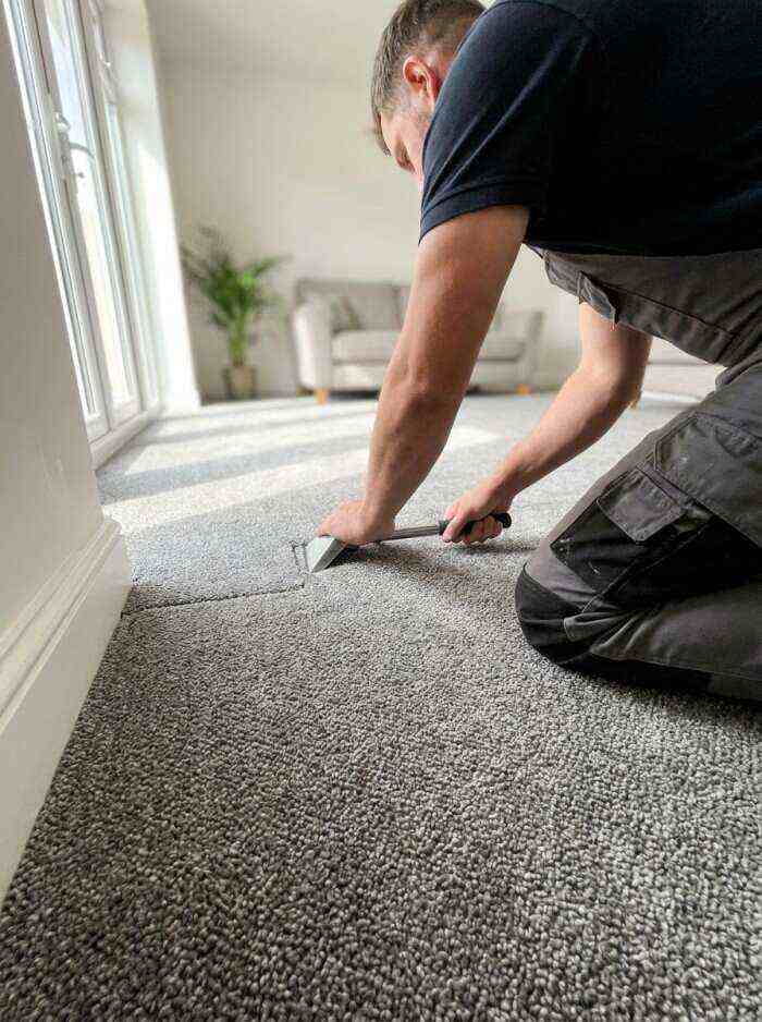 A professional fitter installing grey carpet in a bright, modern living room